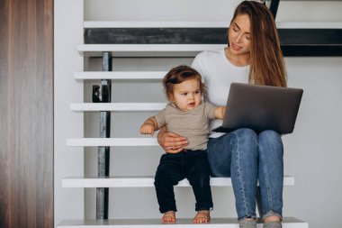 Küçük oğluyla birlikte laptopta çalışan genç bir anne.