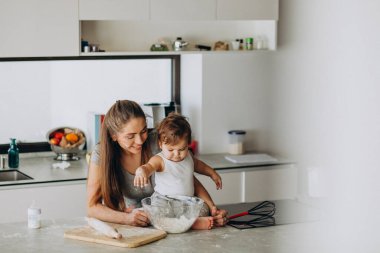 Genç anne ve küçük oğlu mutfakta yemek pişiriyor.