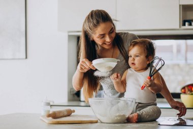 Genç anne ve küçük oğlu mutfakta yemek pişiriyor.