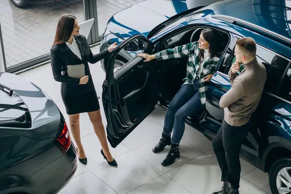 Young couple talking to a sales person in a car showroom