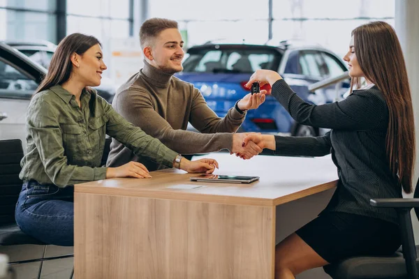 Young couple talking to a sales person in a car showroom
