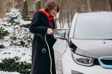 Evinin önünden geçen kadın elektro arabayı şarj ediyor.