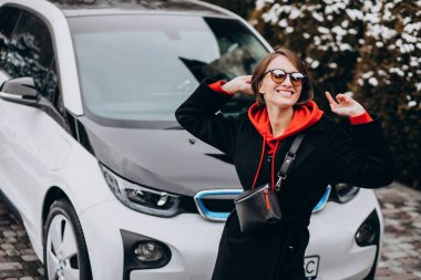 Evinin önünden geçen kadın elektro arabayı şarj ediyor.
