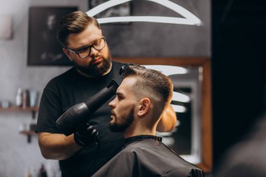 Berber dükkanındaki yakışıklı adam saç şekillendiriyor.