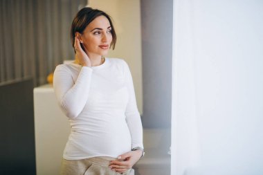 Genç hamile kadın pencerenin önünde duruyor.