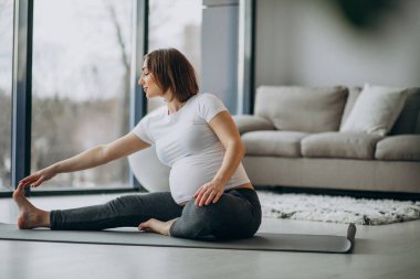 Genç hamile kadın evde yoga yapıyor.