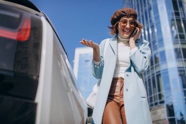 Merkezde elektro arabanın yanında genç bir kadın konuşuyor.