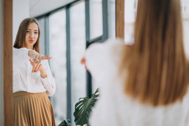 Gündelik kıyafetli güzel bir kadın aynaya bakıyor.