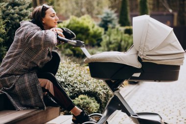 Genç anne arka bahçede bebek arabasıyla yürüyor.