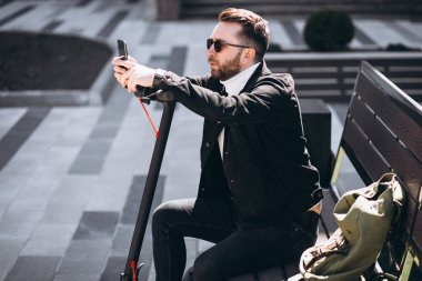 Scooter kullanan yakışıklı adam telefonda internetten alışveriş yapıyor.