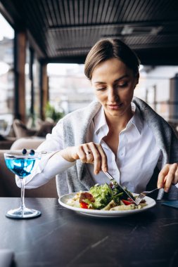 Kokteyl içip kafede salata yiyen bir kadın.