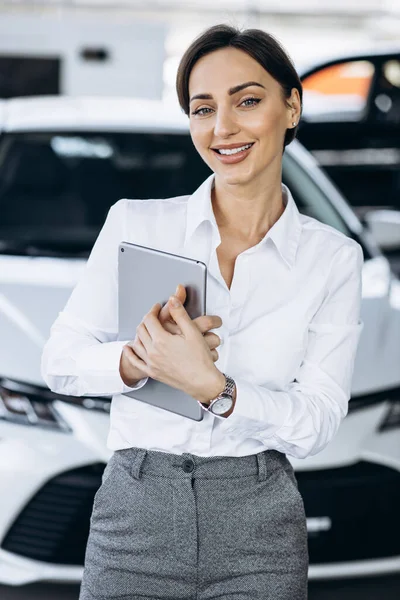 Young saleswoman with tablet in a car showroom