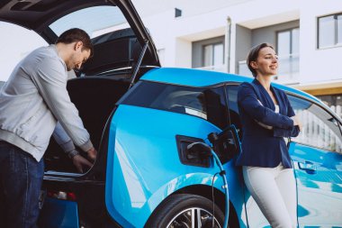 Çift elektrikli arabalarının yanında konuşurken şarj oluyor.