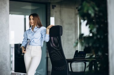 Ofiste dizüstü bilgisayarı tutan genç bir iş kadını.