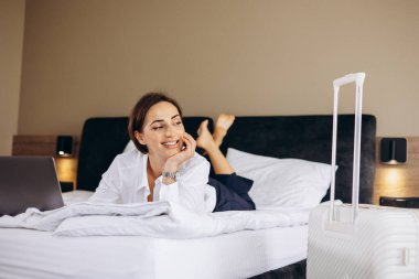 Yatakta yatan ve otel odasında bilgisayarla çalışan bir iş kadını.