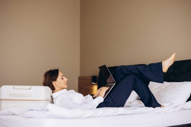 Otelde yatakta yatan ve bilgisayarla çalışan bir iş kadını.