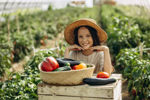 温室に立っている野菜でいっぱいのバスケットを持つ若い女の子 — ストック写真