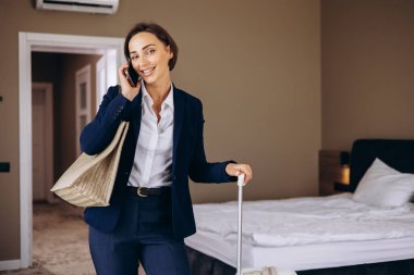 Otel odasında konuşan ve bavullarını taşıyan bir iş kadını.