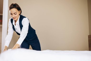 Kadın hizmetçi otel odasında yatak örtüsü hazırlıyor.
