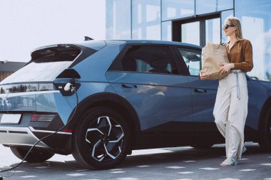 Elektrikli araba şarj edilirken alışveriş yapan kadın.