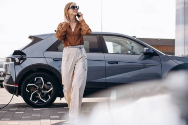 Elektrikli arabasının yanında telefonla konuşan bir kadın.