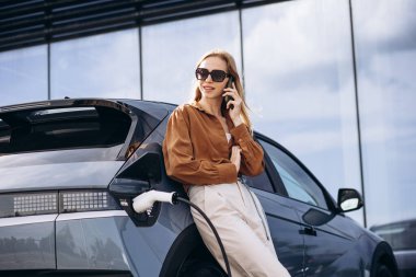 Elektrikli arabasının yanında telefonla konuşan bir kadın.