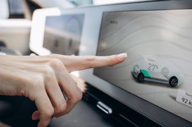 Kadın ekrana dokunuyor ve elektrikli arabasının şarjına bakıyor.