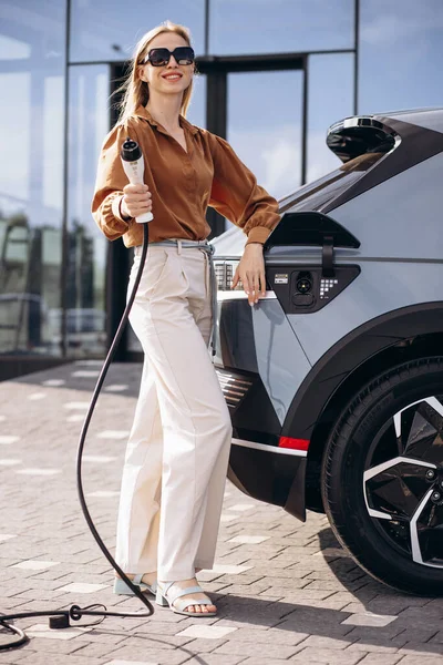 Kadın elektrikli arabaya elektrik kablosu takıyor.