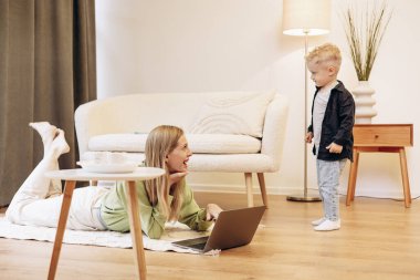 Oğlu oyun oynarken bilgisayarda çalışan bir kadın.