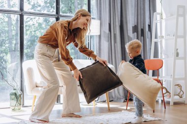 Anne ve küçük oğlu evde yastıklarla oynuyorlar.