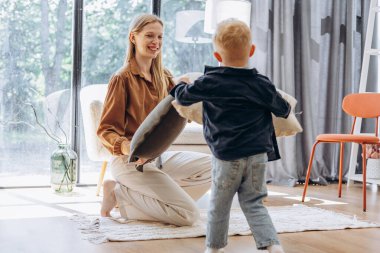 Anne ve küçük oğlu evde yastıklarla oynuyorlar.