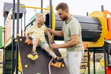 Çocuk babasıyla birlikte çocuk parkında tırmanmayı öğreniyor.