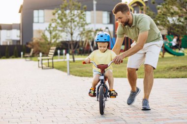 Baba küçük oğluna bisiklet sürmeyi öğretiyor.