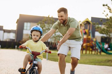 Baba küçük oğluna bisiklet sürmeyi öğretiyor.