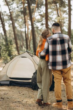 Ormanda çadırlarının yanında yan yana duran iki gezgin.