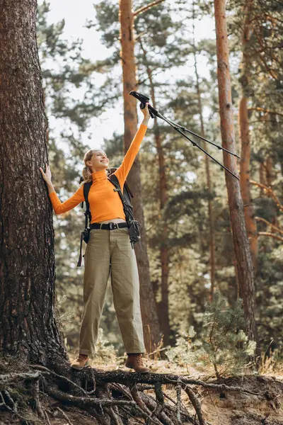 Woman hiking with walking sticks in forest stopped by the tree
