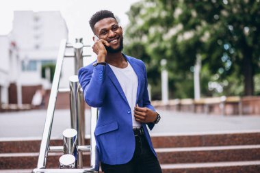 Mavi ceketli Afro-Amerikan adam telefon kullanıyor.