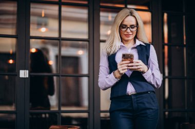 Kafenin dışında telefon kullanan yaşlı bir iş kadını.