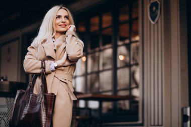 Kafenin dışında ceketli yaşlı bir kadın var.