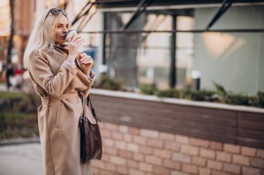 Caddenin dışında kahve içen yaşlı kadın.