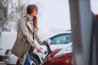 Elektrikli benzin istasyonunda kadın elektro arabayı şarj ediyor.
