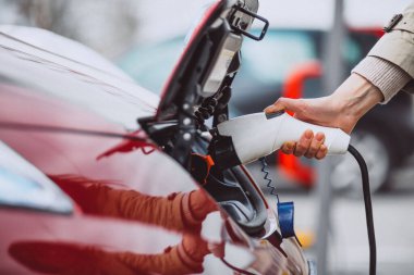 Elektrikli benzin istasyonunda kadın elektro arabayı şarj ediyor.