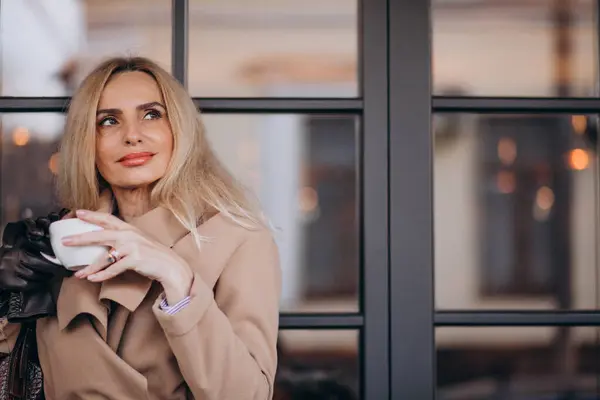 Kafenin dışında kahve içen yaşlı bir kadın.