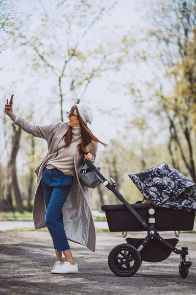 公園で乳母車と歩く若い母親 — ストック写真