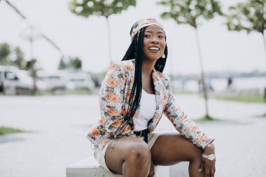 Parktaki bir kayanın üzerinde oturan şık Afrikalı Amerikalı kadın.