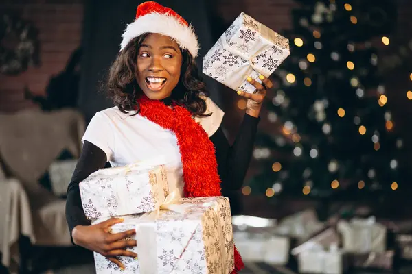 African american woman with presents by the Christmas tree