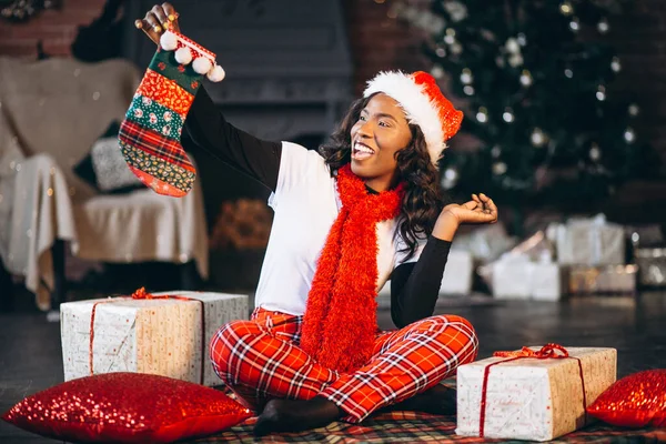African american woman holding christmas presents by the christmas tree