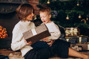 Anne ve küçük oğlu Noel ağacının yanında oturuyor.