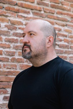 45 yaşında, kel, keçi sakallı ve bıyıklı bir adamın dış görüntüsü.