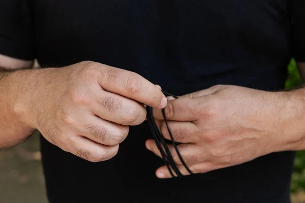 Close-up of the hands of a 45-50 year old man winding the thin cable of headphones. Selective focus